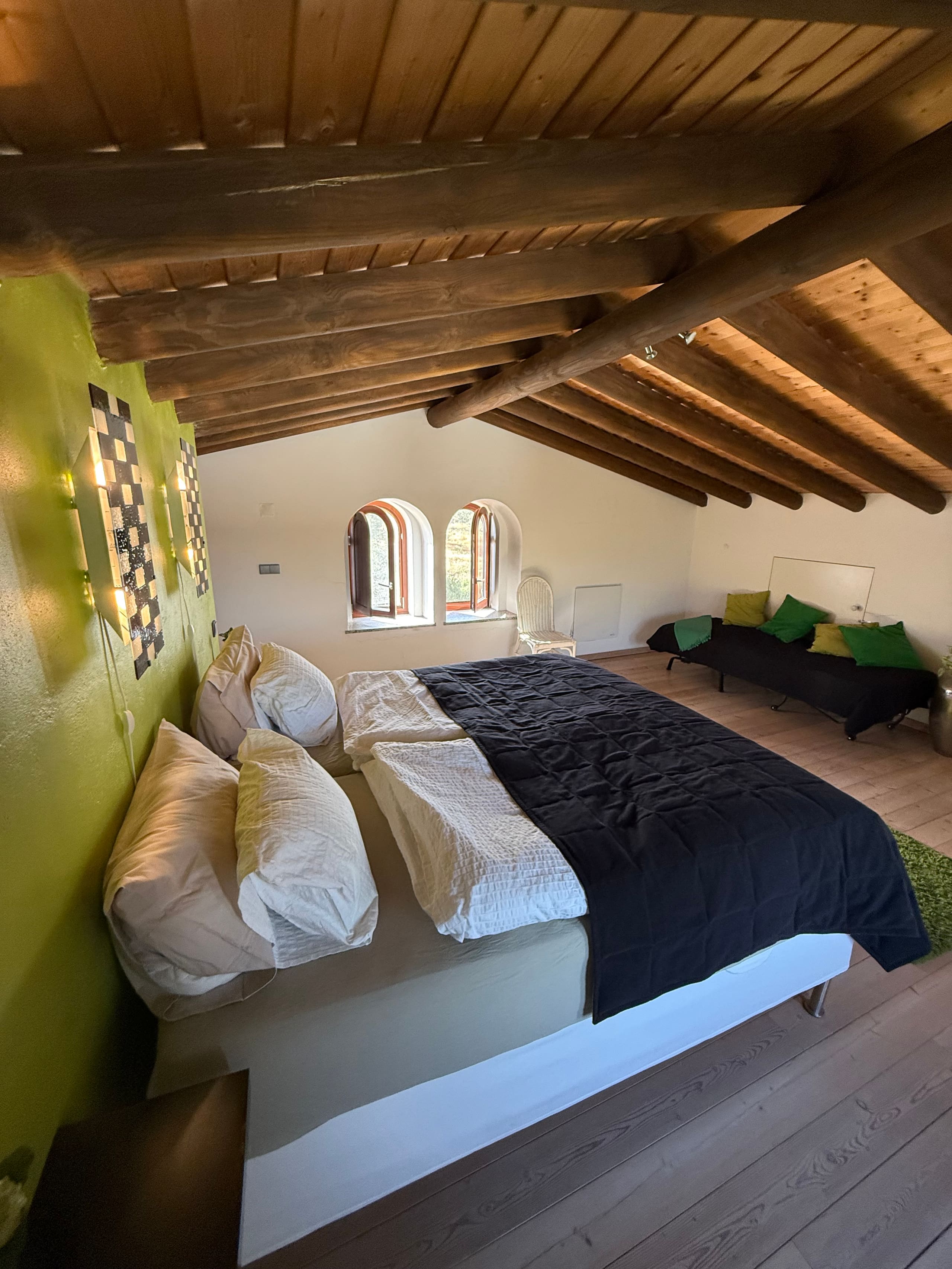 Blick von der Seite auf das Dachgeschoss-Schlafzimmer der Casa Grande mit zwei Rundbogenfenstern und Zusatzbett.