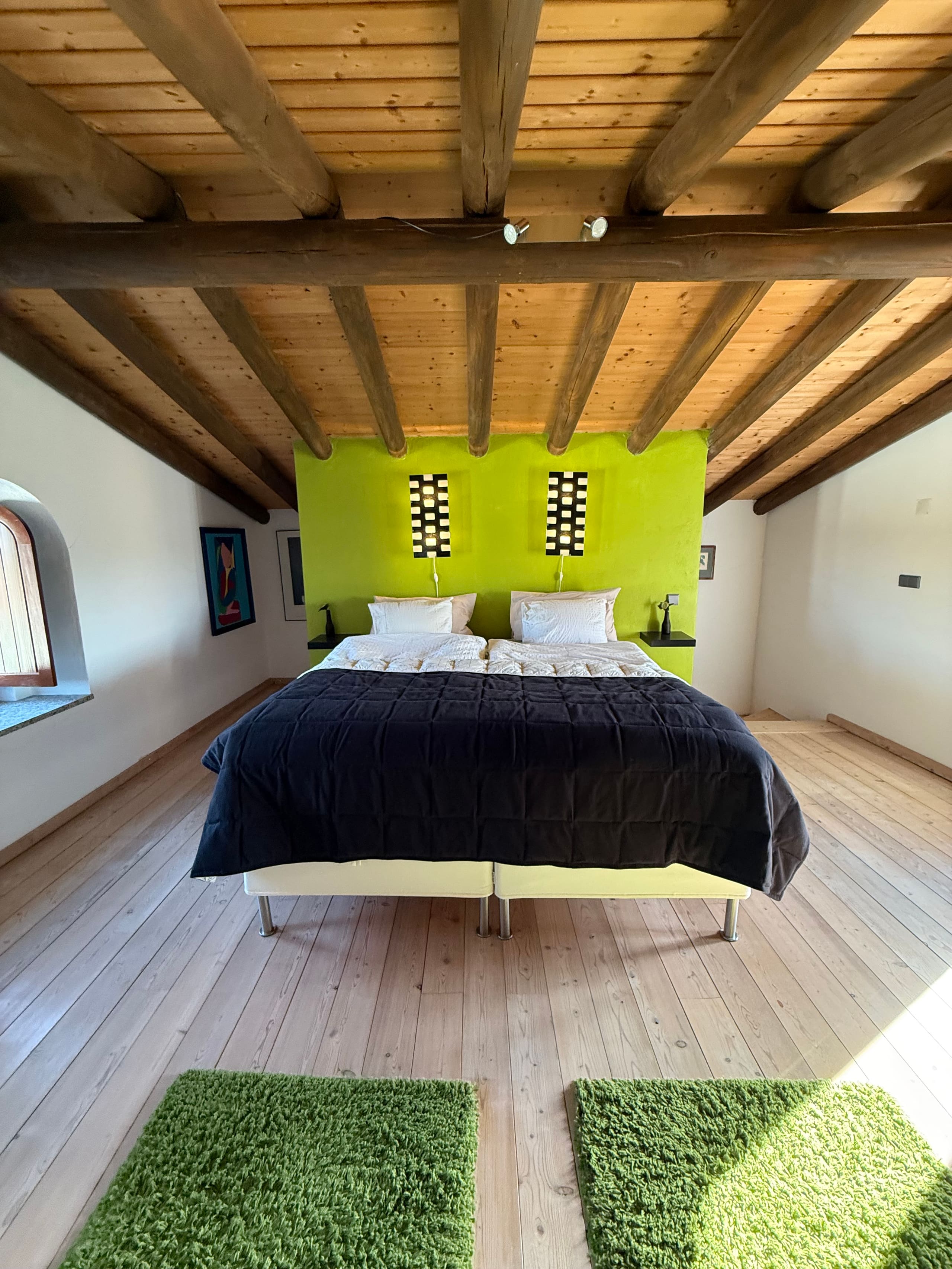 Schlafzimmer mit limettengrüner Wand und Doppelbett unter der Balkendecke des Dachgeschosses der Casa Grande.