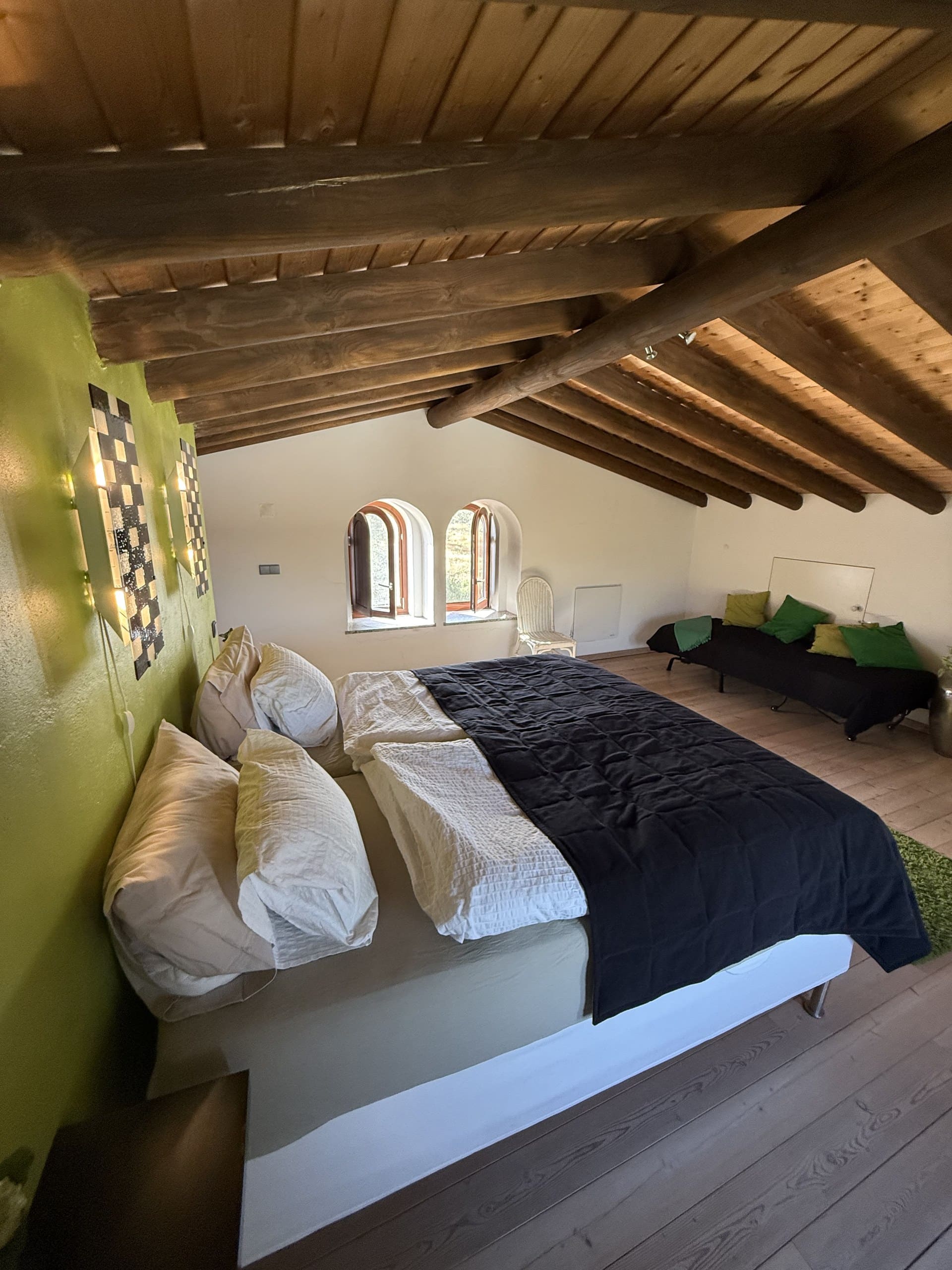 Blick von der Seite auf das Dachgeschoss-Schlafzimmer der Casa Grande mit zwei Rundbogenfenstern und Zusatzbett.