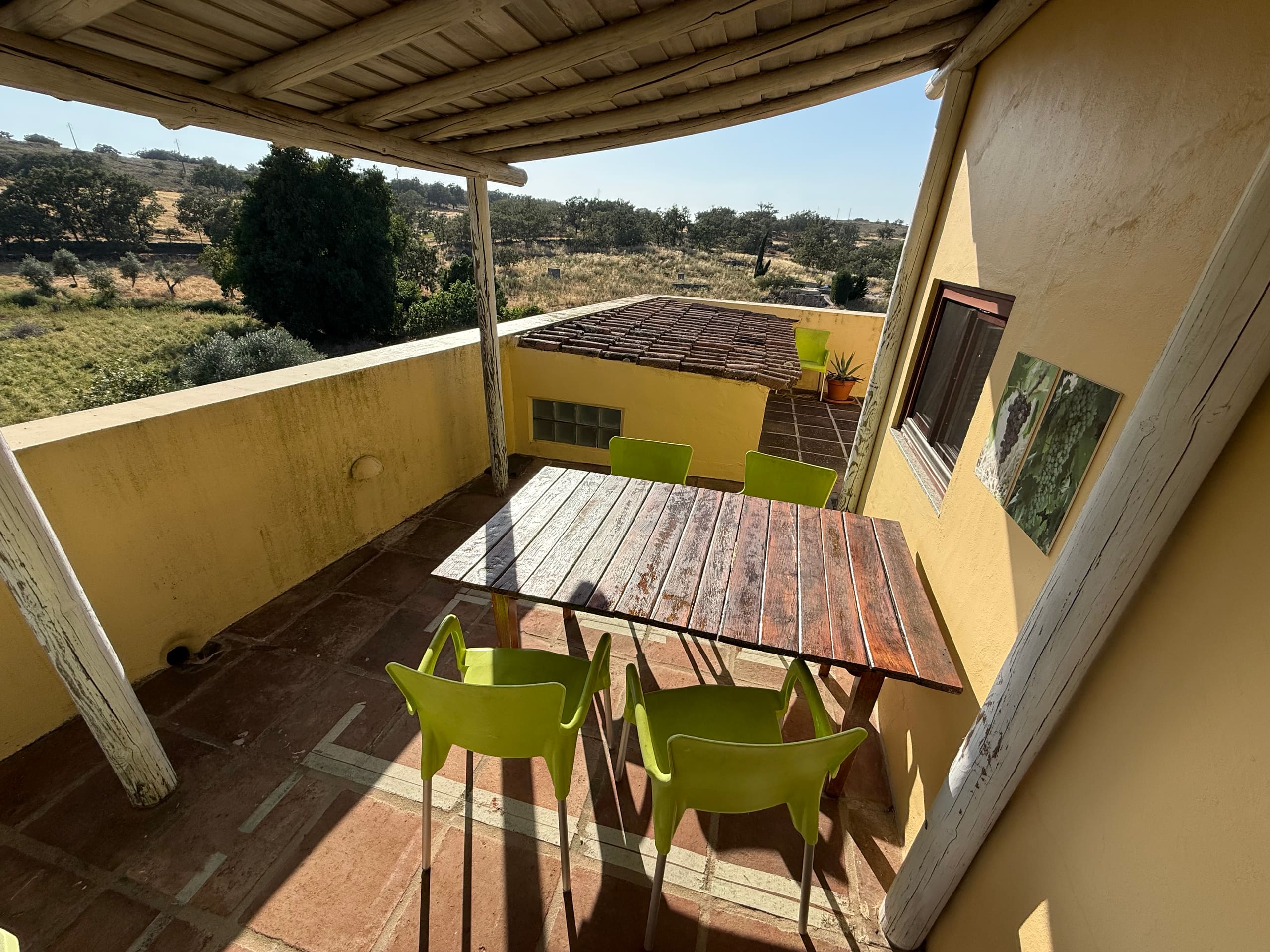 Überdachte Terrasse der Casa Grande mit Holztisch und grünen Stühlen, von oben gesehen.