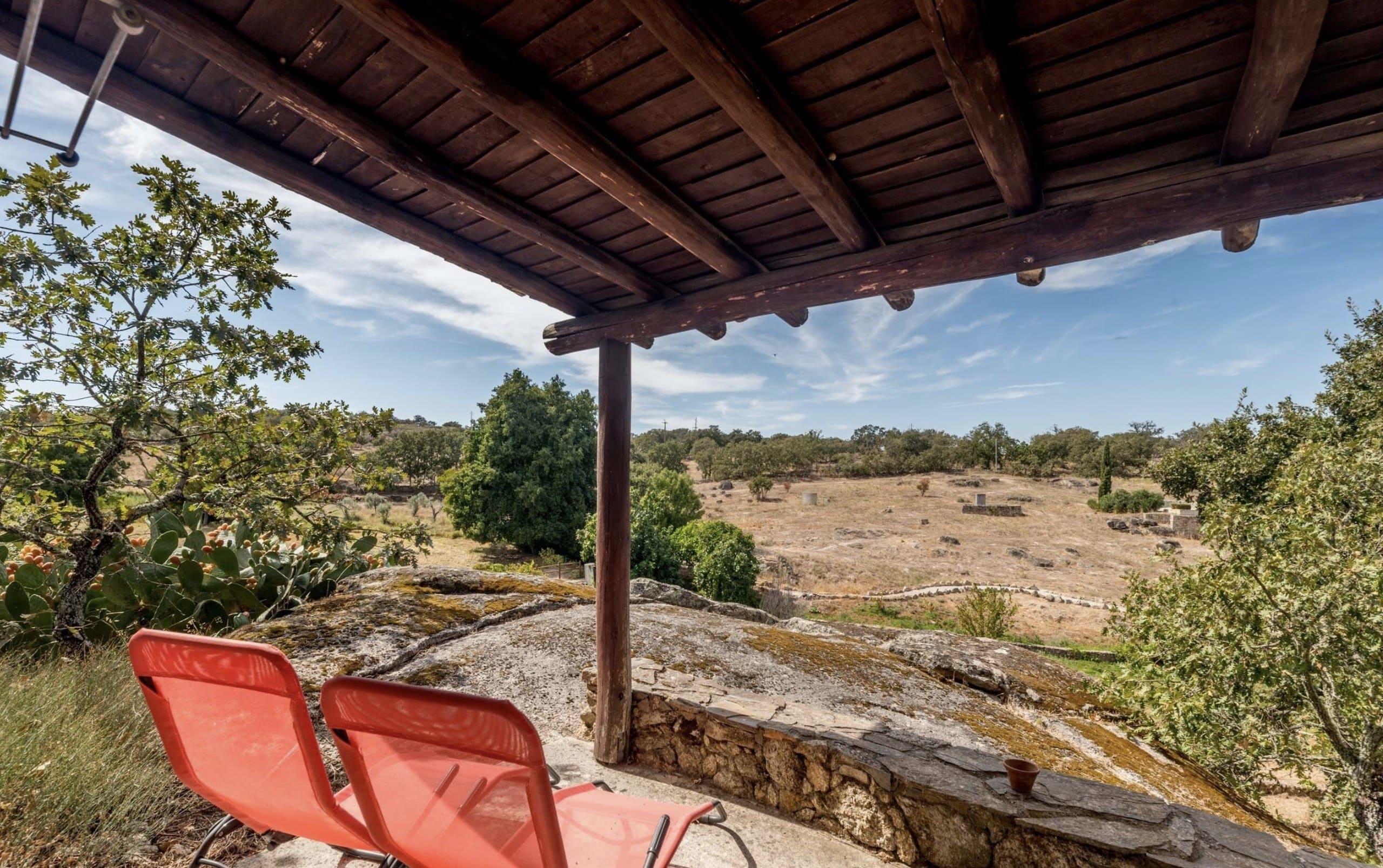 Überdachte Terrasse der Casa Terra auf dem Granitfelsen mit zwei roten Liegestühlen und Blick über die Landschaft.
