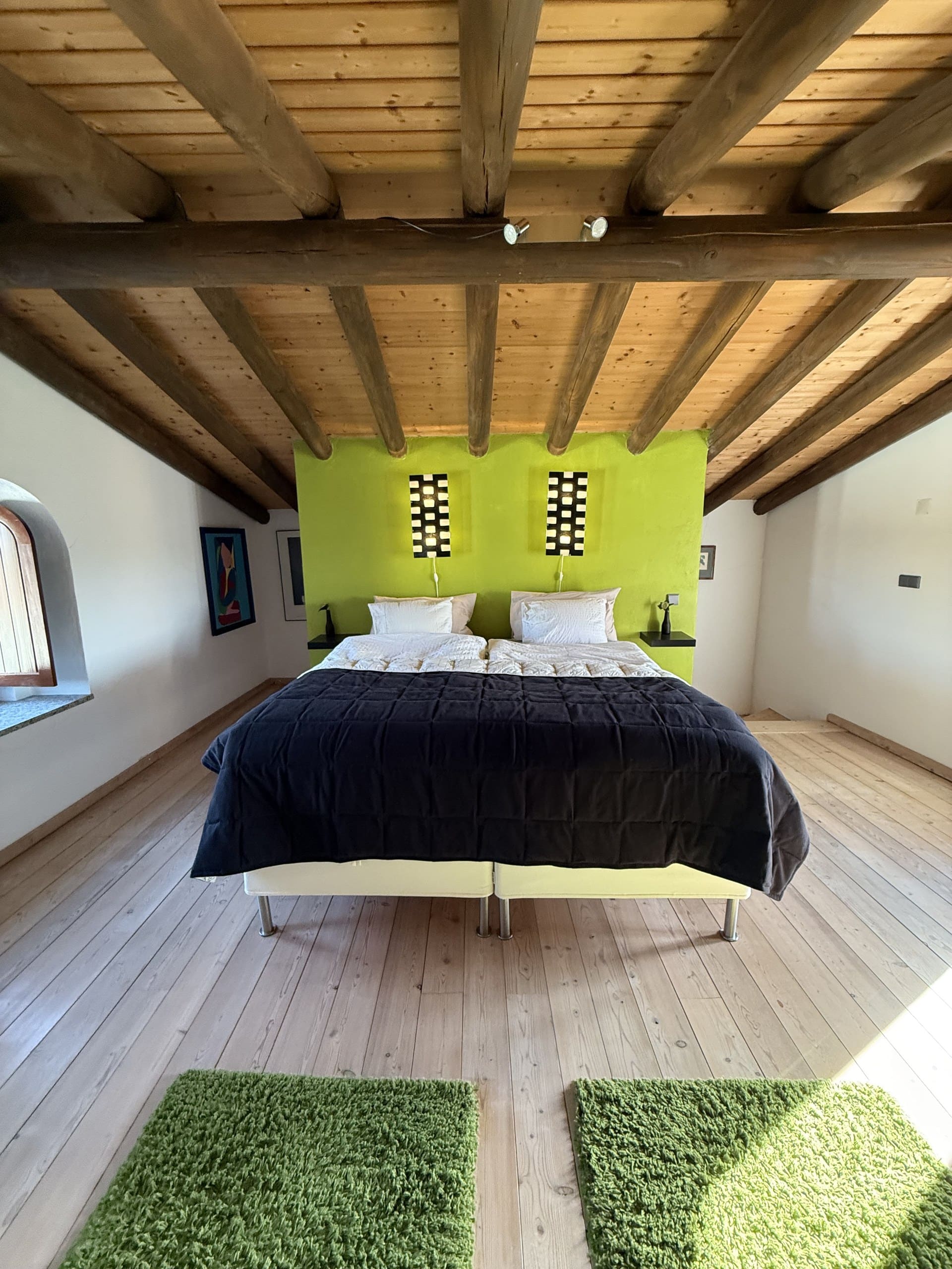 Schlafzimmer mit limettengrüner Wand und Doppelbett unter der Balkendecke des Dachgeschosses der Casa Grande.