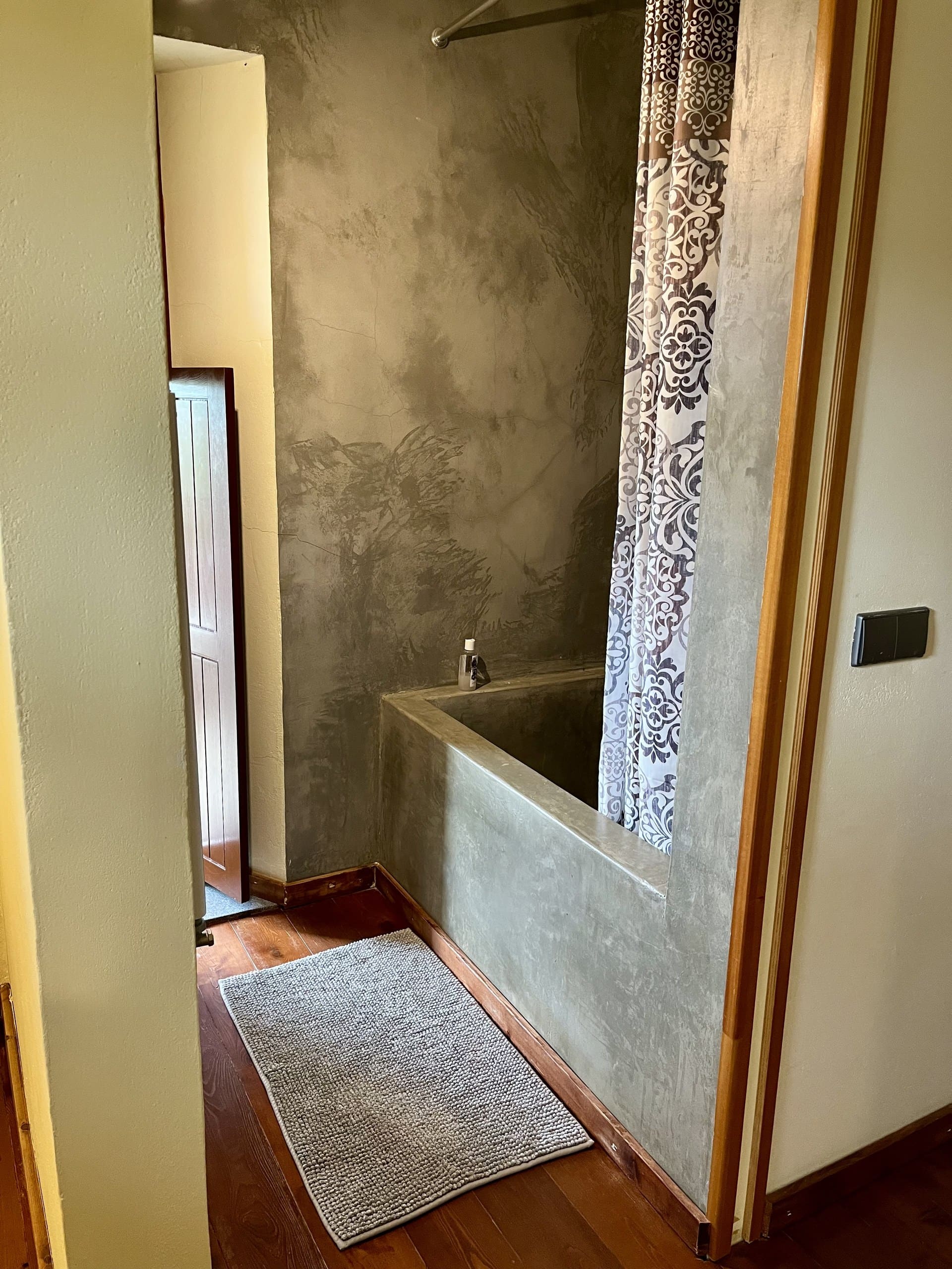 Gemauerte Badewanne mit gemustertem Duschvorhang im Bad der Casa Hridaya.
