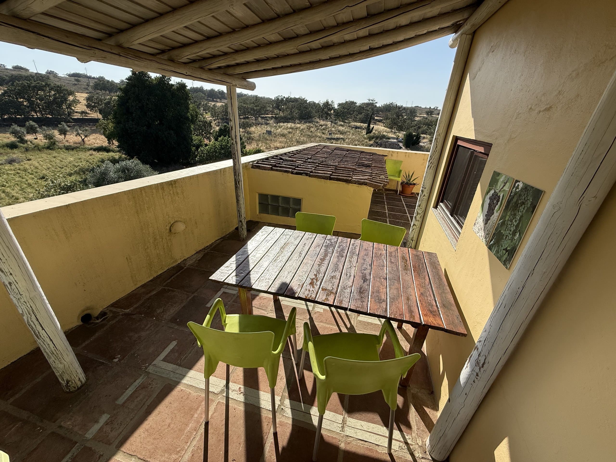 Überdachte Terrasse der Casa Grande mit Holztisch und grünen Stühlen, von oben gesehen.