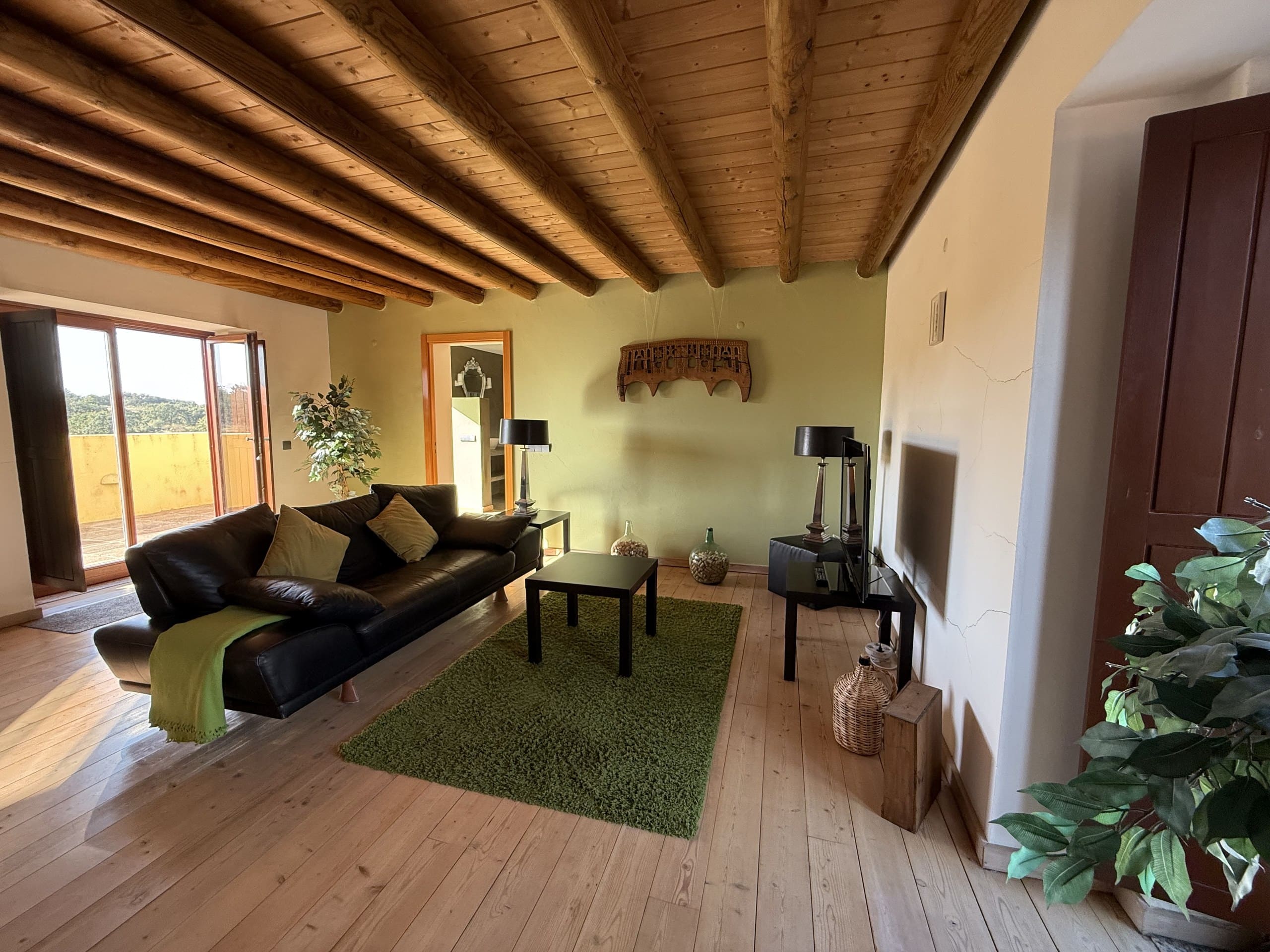 Wohnraum der Casa Grande mit Ledersofa, Holzbalkendecke und offener Tür zur Terrasse.