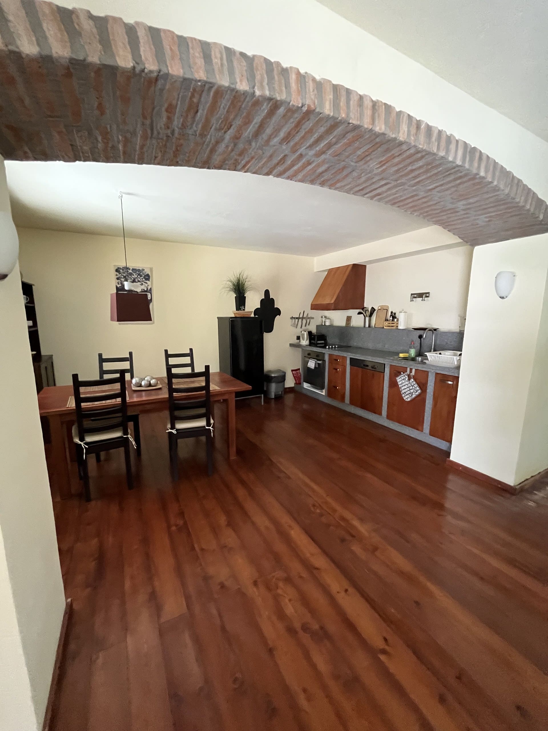 Wohnküche der Casa Hridaya mit Esstisch, gesehen durch den Ziegelbogen.