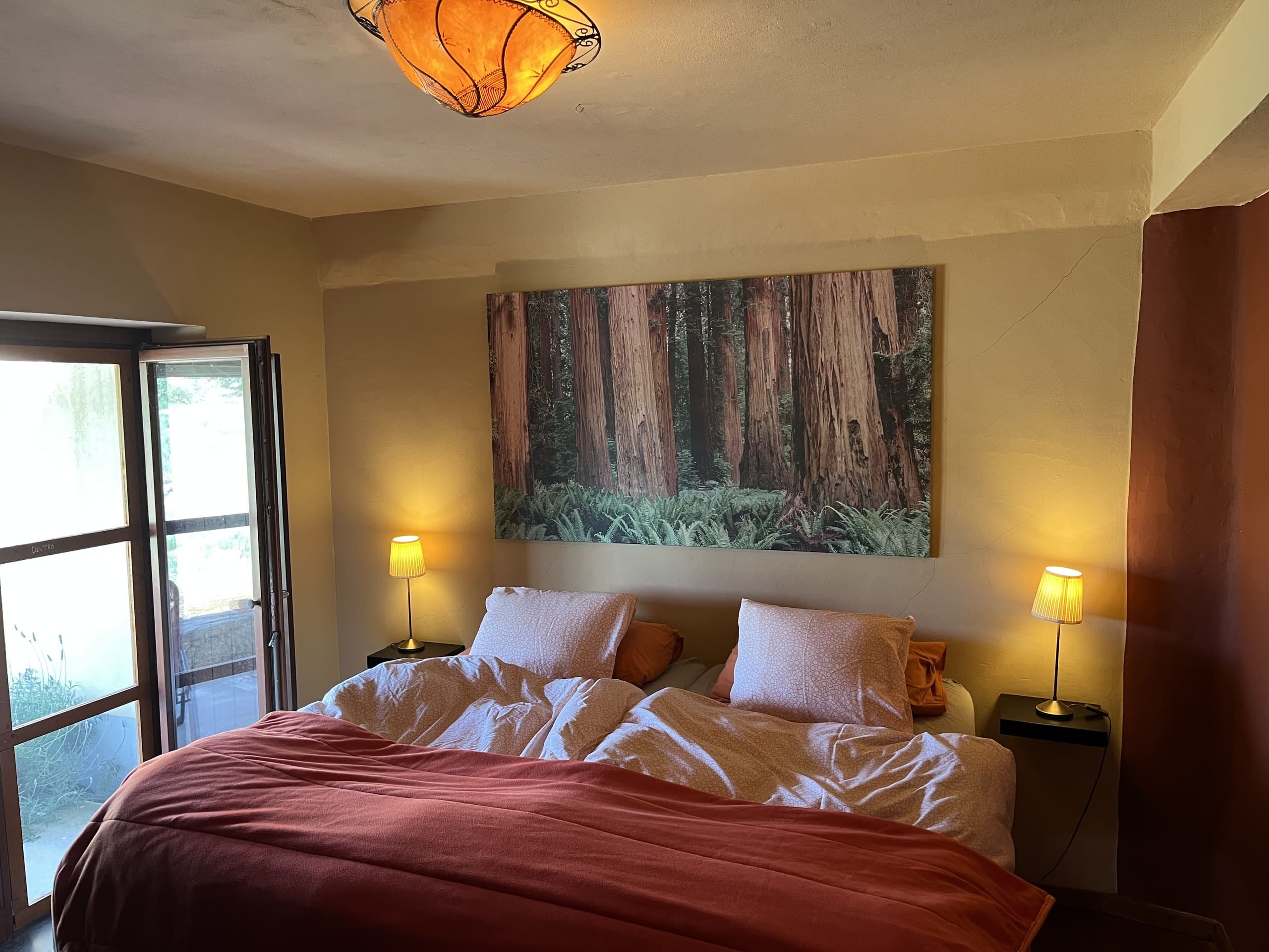 Schlafzimmer der Casa Terra mit Doppelbett, Waldbild über dem Kopfende und Tür zur Terrasse.