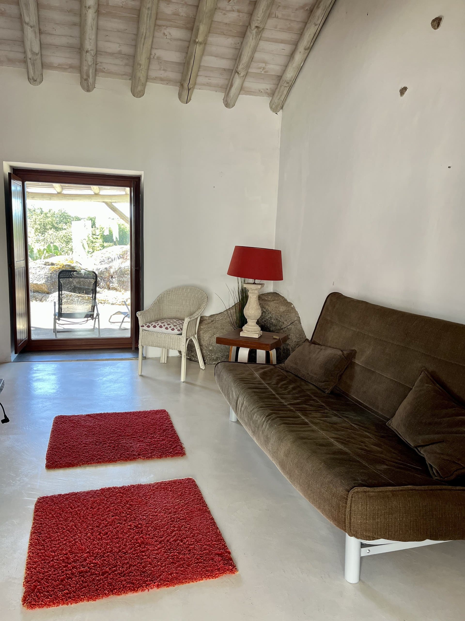 Wohnraum der Casa Amor Perfeito mit Sofa, roten Teppichen und offener Tür zur Terrasse.
