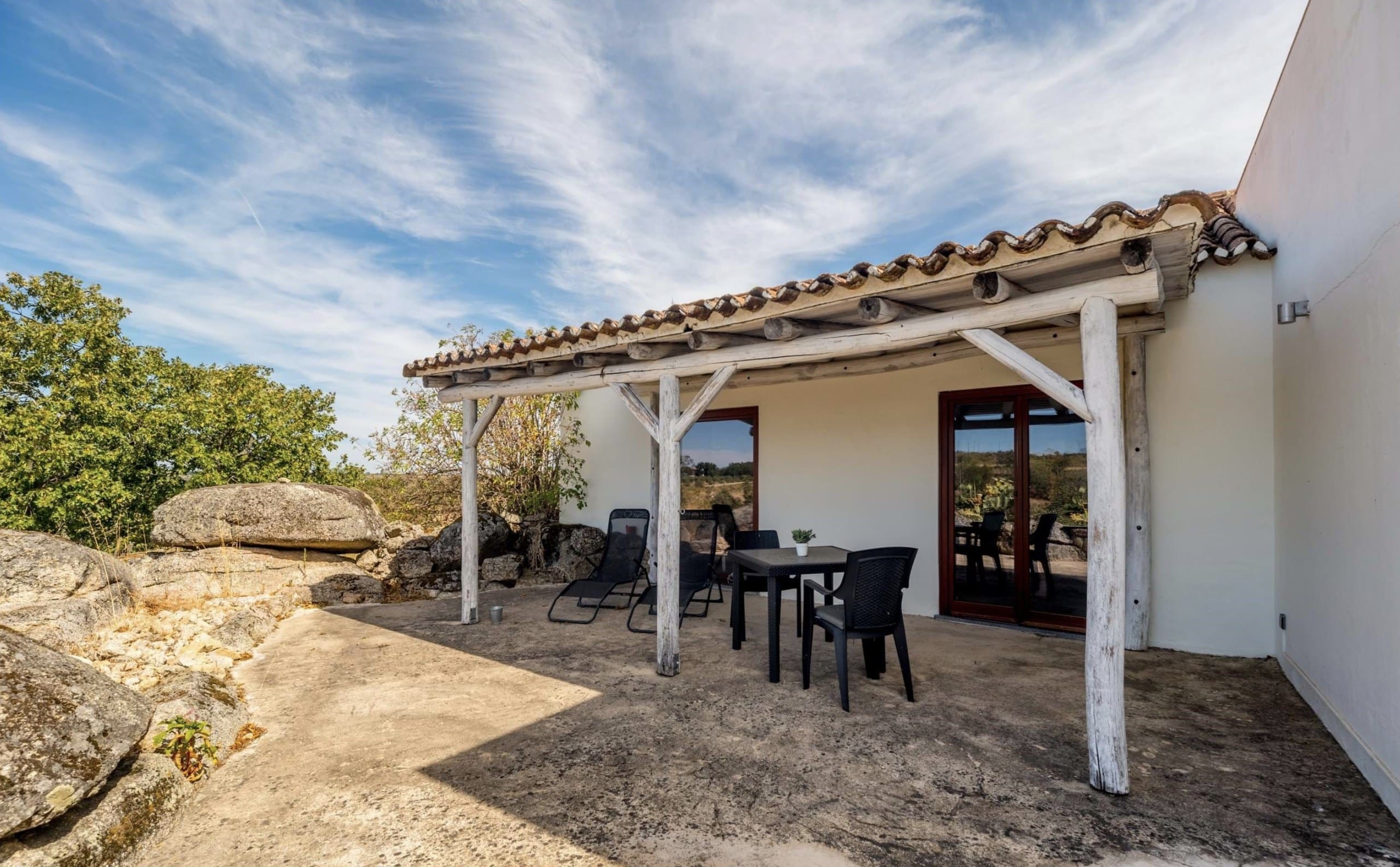Überdachte Terrasse der Casa Amor Perfeito mit Tisch, Stühlen und Sonnenliegen zwischen Granitfelsen.