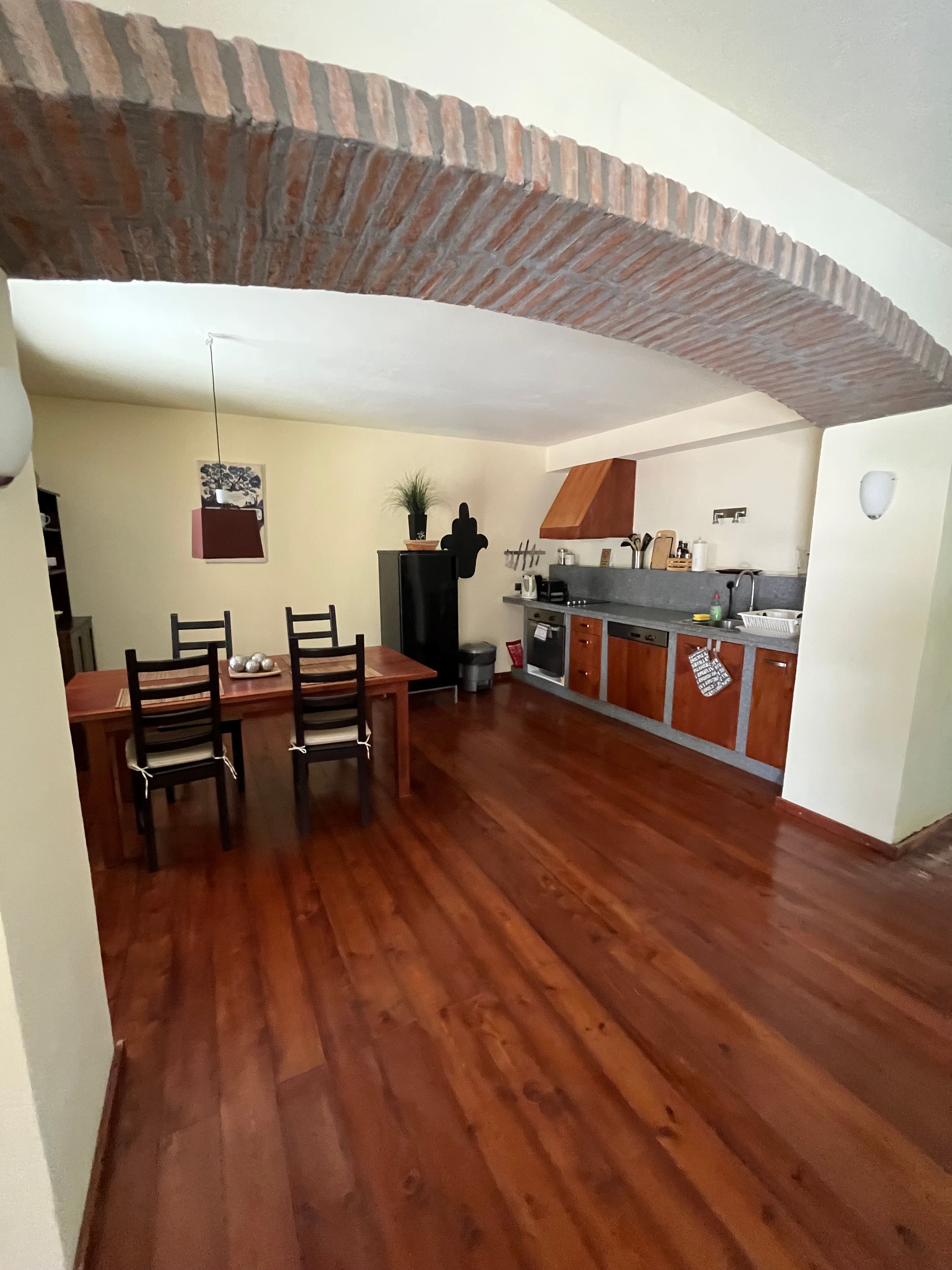 Wohnküche der Casa Hridaya mit Esstisch, gesehen durch den Ziegelbogen.